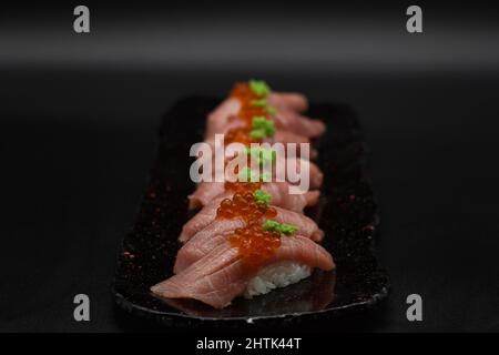 Otoro Thunfisch ist der beste Teil des Thunfischbauch. Köstliche acht japanische Thunfisch-Nigiris auf weißem Reis mit Wasabi und Kaviar serviert. Schwarzer Hintergrund. Stockfoto