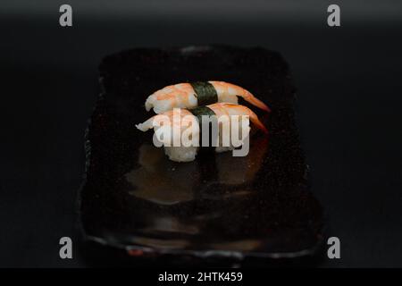 Zwei Einheiten Ebi King Premium Garnelen Nigiris, serviert auf schwarzem Teller auf schwarzem Hintergrund von einem japanischen Restaurantkoch. Stockfoto