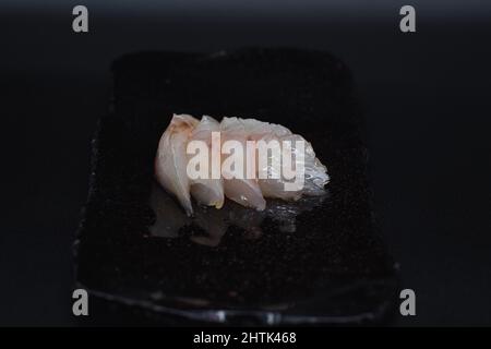 Traditioneller japanischer Sashimi-Schnitt, roher und frischer weißer Fisch in Scheiben geschnitten und auf schwarzem Teller mit schwarzem Hintergrund auf minimalistische Weise serviert. Stockfoto