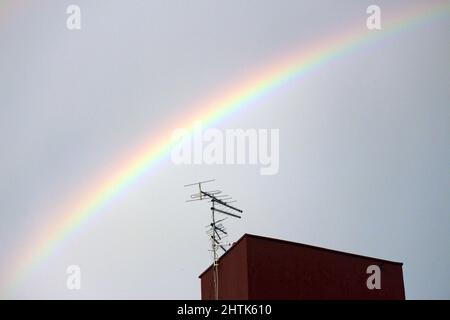 Ein Regenbogen überquert den Himmel über den Details des städtischen Lebens. Antennen, Quellen und Konstruktion. Stockfoto
