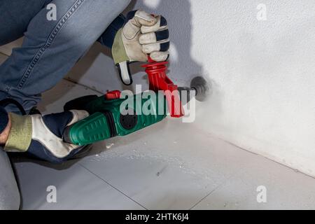 Bohren eines Lochs in eine Betonwand zur Vorbereitung auf die Installation einer Anschlussdose, wo später elektrische Verdrahtung und eine Wandsteckdose installiert werden Stockfoto