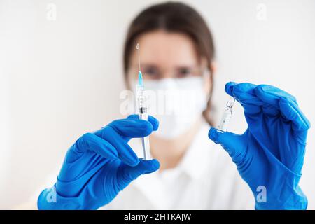 Ein junger Arzt mit einer Spritze und einem Impfstoff in den Händen. Arzt in Innenräumen macht Impfungen. Eine Frau in einem medizinischen Büro. Impfung gegen Influenza Stockfoto