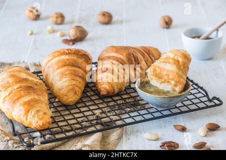 Köstliche französische Croissants auf einem Kühlregal auf weißem Holzhintergrund, ein Stück in Marmelade getaucht Stockfoto