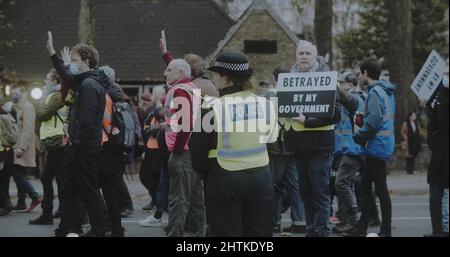 London, Großbritannien - 11 20 2021: Eine diensthabende Polizistin, während eine Schar von beleidigenden britischen Demonstranten auf dem Weg zur Lambeth Bridge vorbei geht. Stockfoto