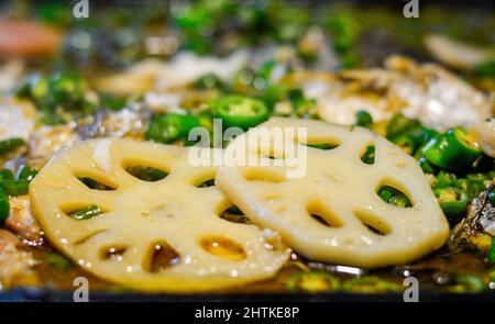 Zwei Scheiben Lotuswurzel auf einem chinesischen heißen Topf mit grünen Chilischoten. Stockfoto