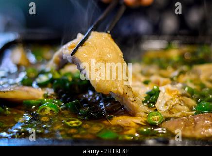 Essstäbchen nehmen Fisch aus einem chinesischen heißen Topf mit grünen Chilischoten auf. Stockfoto