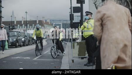 London, Großbritannien - 12 13 2021: Menschen auf der Bridge Street fahren in Westminster mit einem Fahrrad, wobei ein Metropolitan-Polizeibüro im Einsatz ist und eine Gesichtsmaske trägt. Stockfoto