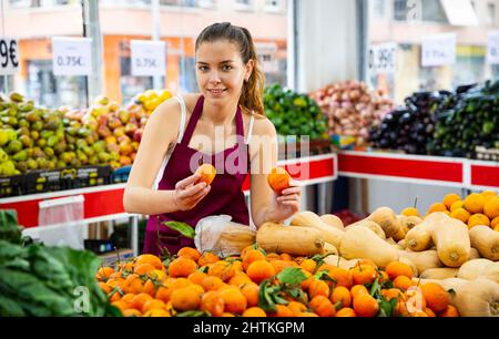 Lächelnde Verkäuferin legt reife Orangen auf die Theke Stockfoto