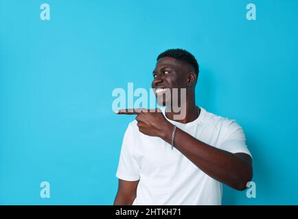 Afroamerikaner zeigen mit dem Finger auf einen isolierten blauen Hintergrund auf die Seite Stockfoto