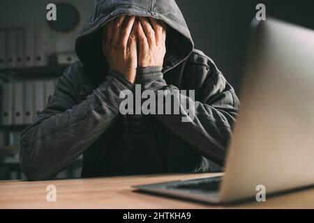 Bedauert Computerhacker, der das Gesicht mit den Händen vor dem Laptop bedeckt, selektiver Fokus Stockfoto