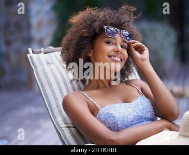 Das ist, wie ich jeden Tag verbringen möchte. Attraktive ethnische Frauen, die sich im Liegestuhl entspannen und ihre Sonnenbrille hochhalten. Stockfoto