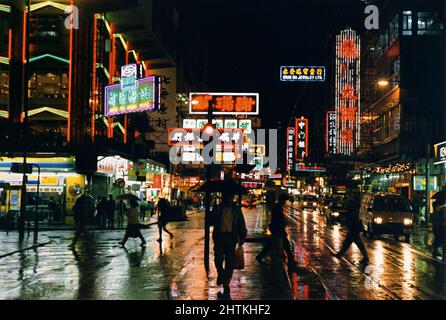 Hennessy Road, Causeway Bay, Hongkong, China: Abendkäufer in einer neonbeleuchteten Straße mit Reflexionen auf den nassen Gehwegen. Stockfoto