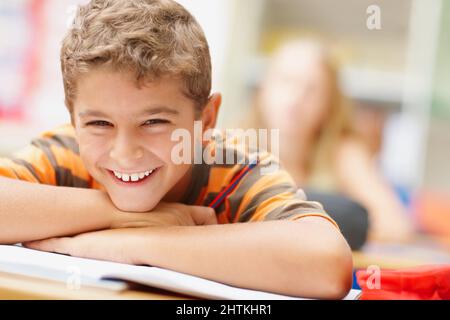 Ich habe alle meine Mathe-Hausaufgaben gemacht. Glücklicher Schuljunge, der seinen Kopf auf seinen Armen ruht und dich anlächelt - Copyspace. Stockfoto