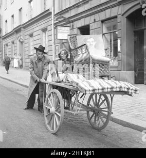 Umzug in die 1940s. Ein Paar schiebt einen Wagen vor sich mit einigen Möbeln darauf. Sie scheinen damit zu kämpfen. Schweden 1943. Kristofferson Ref. C86-4 Stockfoto