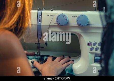 Nahaufnahme der argentinischen kaukasischen Frau, die in ihrem Studio mit blauen Stoffen an der Nähmaschine arbeitet und Modebekleidung entwirft. Stockfoto