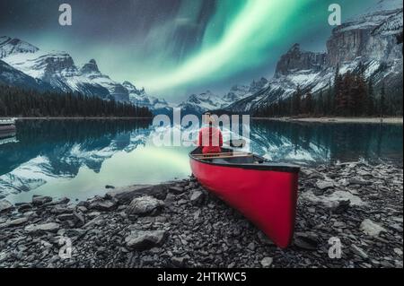 Aurora Borealis über der Spirit Island mit einer Reisenden Frau, die auf einem roten Kanu auf dem Maligne Lake im Jasper National Park, ab, Kanada sitzt Stockfoto