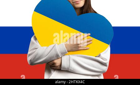 Ein Mädchen hält sich mit der Flagge der Ukraine und hinter ihr die Flagge der Russischen Föderation ein Herz an die Brust. Stockfoto