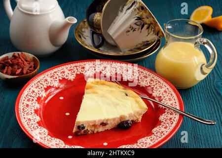 Hausgemachter Hüttenkäse-Käsekuchen auf rotem Teller mit Zitronenkuchen, Tee und Goji-Beeren aus der Nähe Stockfoto
