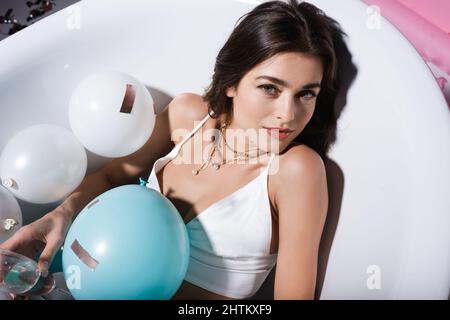 Man hat einen Blick auf die Frau, die in der Badewanne mit Luftballons lag und ein Glas Champagner in der Hand hielt Stockfoto