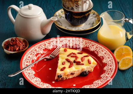 Leckerer selbstgemachter Käsekuchen mit Rosinen, Zitronenkurz und Goji-Beeren auf rotem Teller aus der Nähe Stockfoto