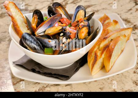 Gekochte Muscheln in einer Schüssel mit Brühe und Knoblauchtoast. Stockfoto