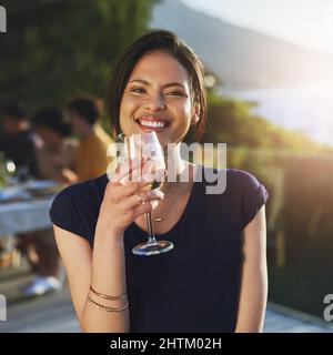 Er ist so fein wie der knackige Wein, den sie trinkt. Aufnahme einer attraktiven jungen Frau, die mit ihren Freunden im Hintergrund ein Glas Wein im Freien genießt. Stockfoto