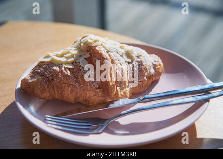 Mandelsüßes Croissant auf einem Teller auf dem Tisch in einem Café. Stockfoto