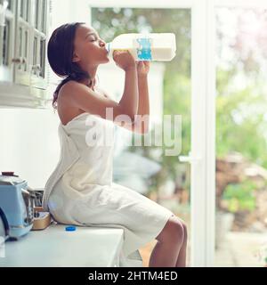 Milch tut meinem Körper gut. Eine junge Frau, die Milch direkt aus der Flasche trinkt, während sie auf der Küchentheke sitzt. Stockfoto