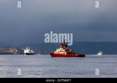 Schlepper BB Worker in Byfjorden, außerhalb des Hafens von Bergen, Norwegen Hurtigrute Skipet Vesterålen im Hintergrund Stockfoto