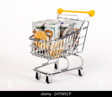 Supermarkt-Trolley mit gerollten Dollarnoten und Münzen. Einkommen und Geld durch Shopping-Konzept ausgegeben. Hochwertige Fotos Stockfoto