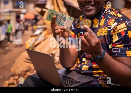 Nahaufnahme der Hände eines afrikanischen Jungen, der eine Bitcoin- und Ethereum-Münze und eine 5000 CFA-Franc-Note hält. Digitales Zahlungsmittel Tin Africa-Konzept Stockfoto