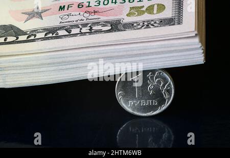 Russische Rubel-Münze durch Stapel von Dollarscheinen zerschlagen, steht das Rubel-Geld unter dem Druck der Geopolitik. Konzept der Abwertung des Rubels, Inflation in Russland Stockfoto