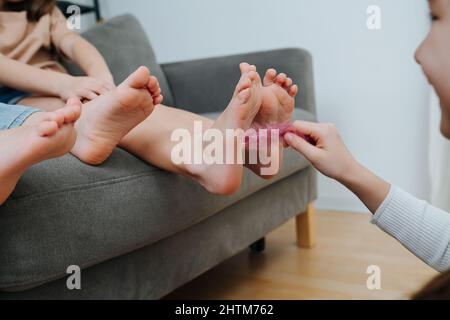 Kinderfüße, die von einem lachenden Mädchen mit einer rosa Feder gekitzelt werden. Konzentrieren Sie sich auf die Füße. Stockfoto