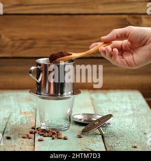 Die Hand der Frau, die gemahlenen Kaffee in einen französischen Tropfmetallfilter legt, der Kaffee macht Stockfoto