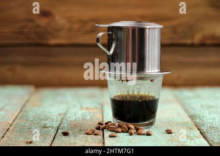 Vietnamesischer schwarzer Kaffee, gebraut in französischem Tropffilter auf türkisfarbenem Holztisch-Copyspace Stockfoto