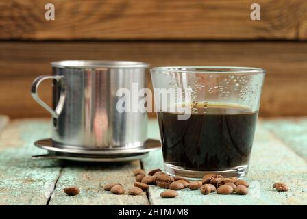 Vietnamesischer Kaffee, der in französischer Tropfenfilter auf einem türkisfarbenen Holztisch aus der Nähe gebraut wird Stockfoto