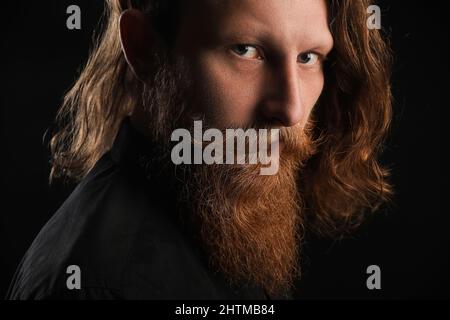 Porträt eines jungen bärtigen Mannes auf schwarzem Hintergrund, Nahaufnahme Stockfoto