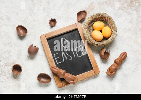 Tafel mit Wort OSTERN, Schokoladenhasen und Eiern auf hellem Hintergrund Stockfoto