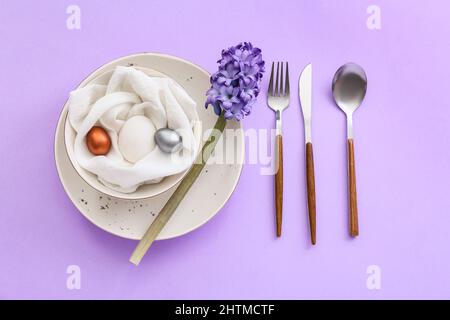 Tischeinstellung mit Ostereiern und Blumen auf lila Hintergrund Stockfoto