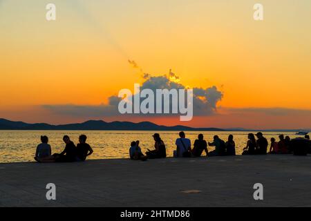 ZADAR, KROATIEN - 14. SEPTEMBER 2016: Das sind die Silhouetten der Menschen am Stadtdamm bei Sonnenuntergang. Stockfoto