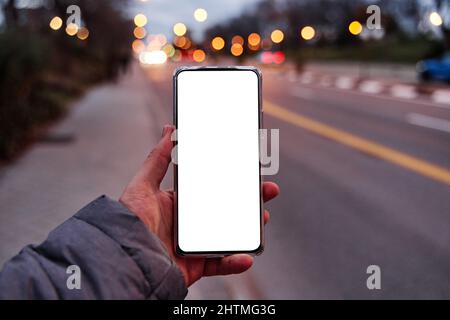 Hand hält Smartphone mit leerem Bildschirm mit Kopierplatz für Ihr Design oder Logo, Mockup von Handy, Abend City Street auf dem Hintergrund, Boke Stockfoto