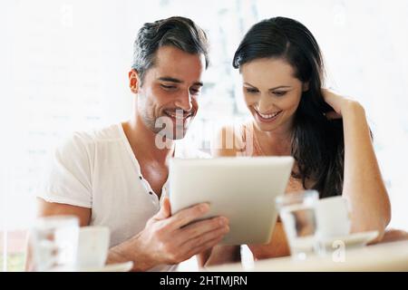 Wi-Fi mit meinem Wifey. Aufnahme eines jungen Paares, das während eines Kaffeetrints seine Tablette benutzte. Stockfoto