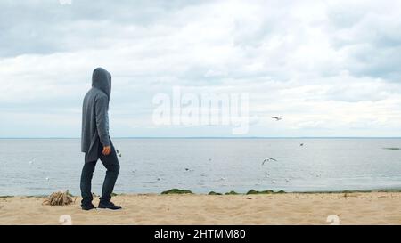 Seitenansicht eines Mannes, der auf den Fluss schaut und Vögel, die am Himmel fliegen. Männchen, das am sandigen Seeufer steht und in die Ferne auf hoch aufragende Möwen blickt. Stockfoto