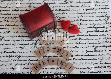 Kleine rote Brust mit Vintage-Schlüssel und zwei roten Herzen auf Schriftpapier mit den Worten 'Schlüssel zu meinem Herzen'. Das Konzept des Valentinstag. Stockfoto