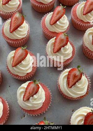 Rosafarbene Kuchen mit Creme und einem halben Stück Erdbeere darauf Stockfoto