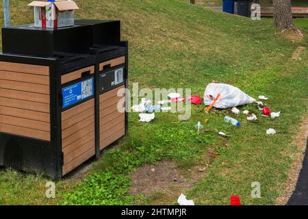 Recycelbarer Müll, der auf dem Rasen neben Recyclingbehältern im öffentlichen Park weggeworfen wird. Stockfoto