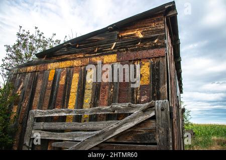 Alte verwitterte Holzscheune mit antiken Wyoming-Nummernschildern, die zum Schutz und zur Dekoration mit dem alten Korallentor an der Wand genagelt wurden Stockfoto