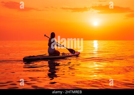 25. Juni 2021. Anapa, Russland. Frau auf dem Stand Up Paddle Board am ruhigen Meer mit Sonnenuntergang oder Sonnenaufgang. Weibchen auf Red Paddle SUP-Board und Sonnenuntergang. Stockfoto