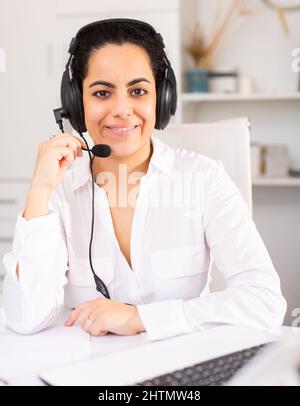 Lächelnde Sprecherin, die mit dem Kunden über das Headset im Büro des Unternehmens spricht Stockfoto
