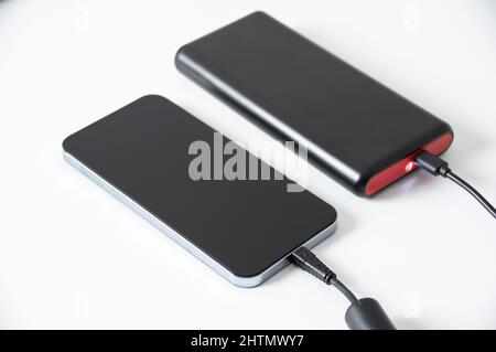 Das Telefon wird über die Powerbank auf einem weißen Tisch aufgeladen. Stockfoto